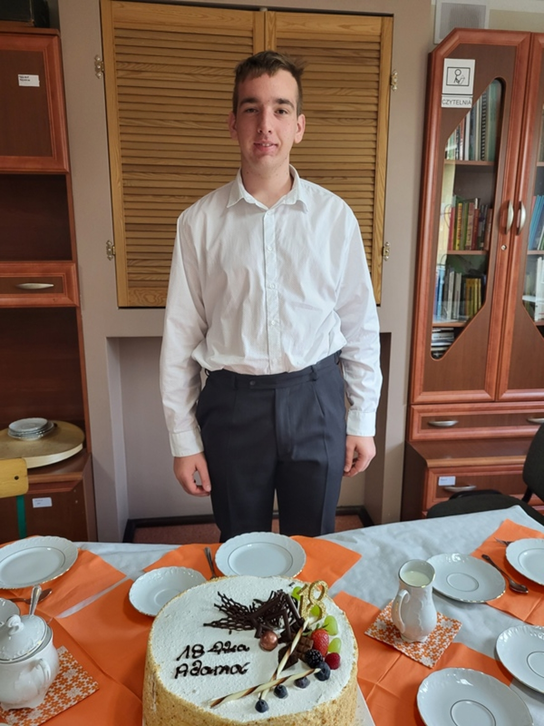 2. Adam przygotowuje się do uroczystości, stoi za stołem a przed nim tort