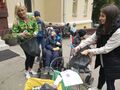 Grupa osób znajduje się przed budynkiem szkoły. Dwie osoby segregują śmieci do worków odpowiedniego koloru 