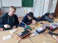16. Trzech uczniów siedzi przy szkolnych ławkach. Wszyscy pracują w drewnie. Jeden wypala wzory drugi wbija gwoździe trzeci dekoruje drewniane