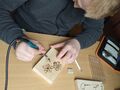 chłopiec siedzi w ławce w klasie i za pomocą wypalarki rysuje wzór kwiatów na drewnie