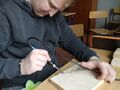 chłopiec siedzi w ławce w klasie i za pomocą wypalarki rysuje wzór swiateczny na drewnie