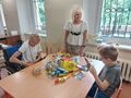 Pani Dyrektor chłopiec i dziewczynka oglądają przy stole prezenty w klasie