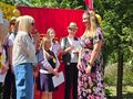 16.Na scenie uczestnicy kobieta w kwiecistej sukni przed nią kobieta mówi do mikrofonu 