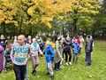 9. Uczniowie i nauczyciele stoją na boisku szkolnym w tle drzewa i kolorowe liście 