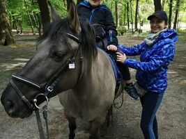 Oliwier ćwiczy równowagę podczas jazdy na koniu stępem, chłopiec siedzi na koniu, obok stoi hipoterapeutka i asekuruje
