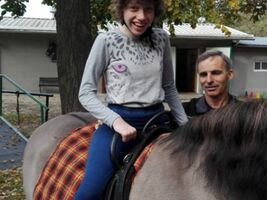 dziewczynka siedzi na grzbiecie konia o imieniu Hejnał, obok asekuruje hipoterapeuta