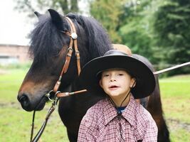 chłopiec w kapeluszu stoi obok konia, uśmiecha się