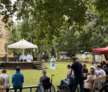 rodzicie uczniowie i nauczyciele siedzą w ławkach w parku na mszy świętej