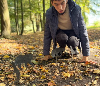 Uczeń jest w parku, kuca i patrzy na tekturowe zwierzątka