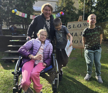 Pani nauczycielka stoi z trzema uczniami. Jeden z uczniów trzyma dyplom, a obok siedzi na wózku dziewczynka_
