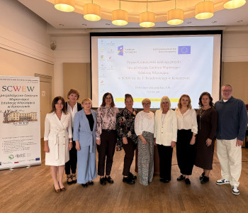 Grupa ludzi pozuje do zdjęcia stoją obok siebie na sali konferencyjnej w tle prezentacja oraz baner scwew